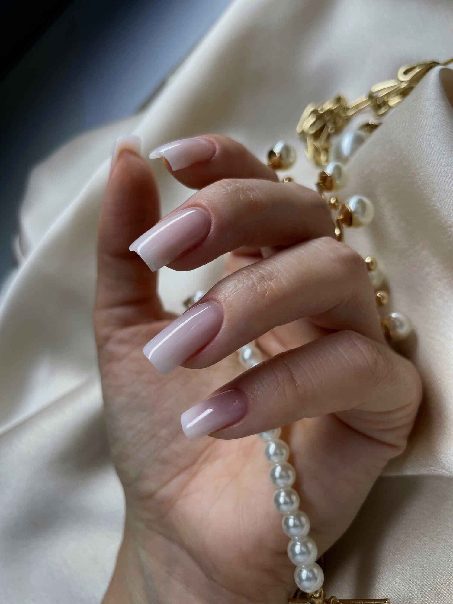 Milky pink almond nails styled with a pearl bracelet and gold jewellery