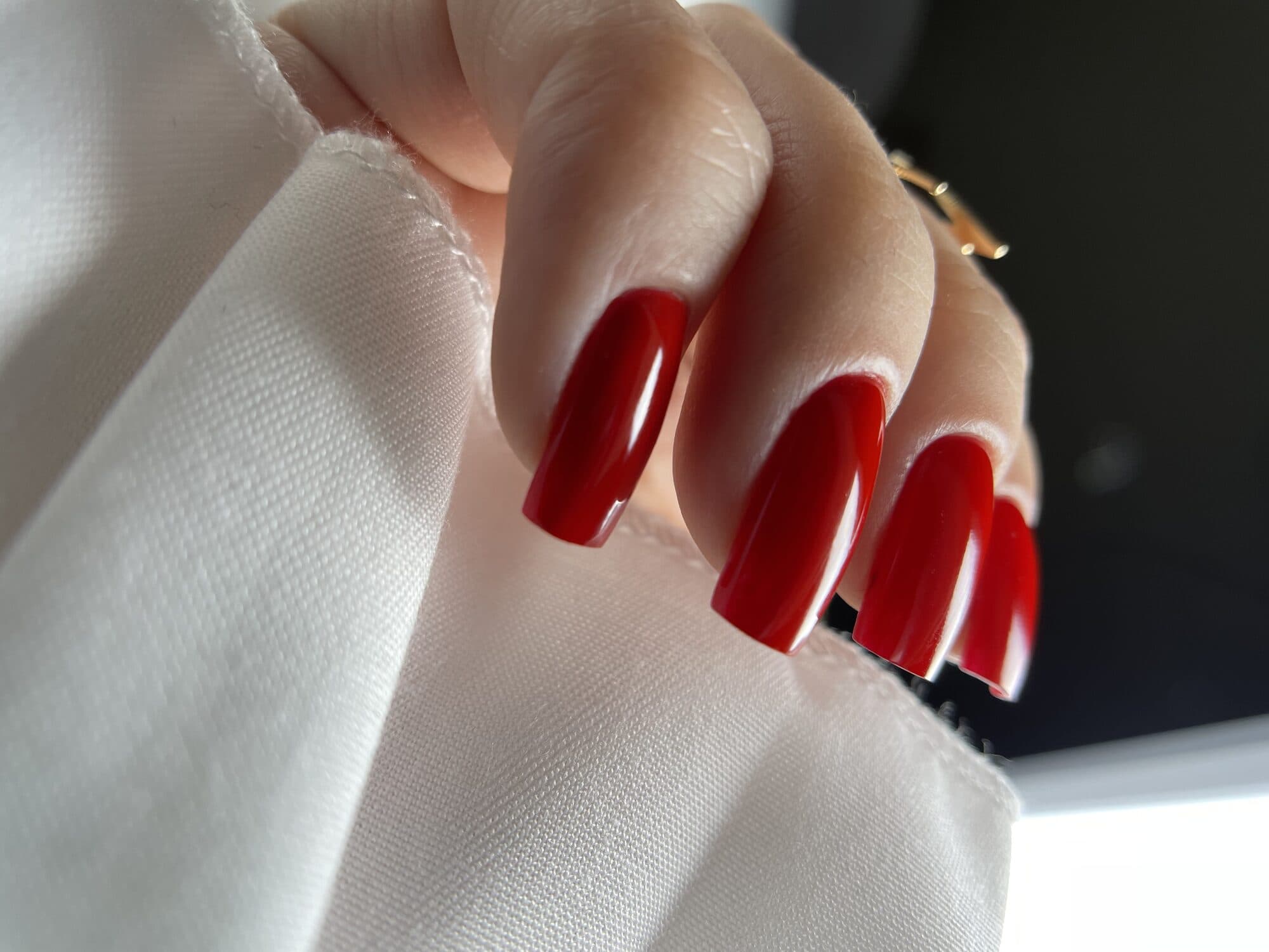 Bright red square nails against a white shirt